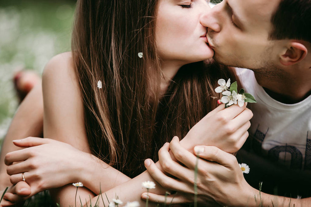 Młoda kochająca para na zewnątrz siedzi na trawie, przytulanie i całuje się nawzajem. - Zdjęcie, obraz