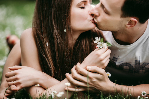 junges Liebespaar im Freien sitzt auf Gras, umarmt und küsst sich. - Foto, Bild