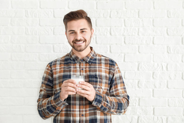 Handsome man with glass of tasty milk on white brick background - Foto, Bild