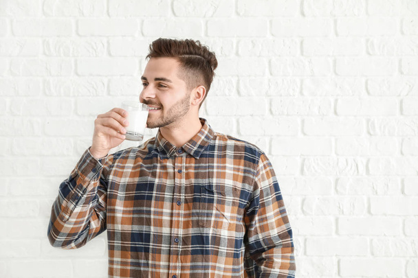Hombre guapo bebiendo leche sabrosa sobre fondo de ladrillo blanco
 - Foto, Imagen