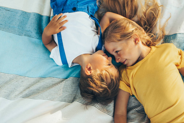 Horizontal top view of adorable children lying on the blanket, looking to each other. Happy little boy and little girl enjoying summertime in the park. Kids playing outdoors. Sister and brother - Foto, imagen