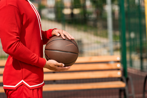 częściowy widok koszykarz trzyma piłkę w pobliżu drewnianej ławce - Zdjęcie, obraz