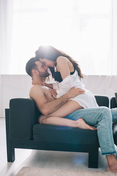 shirtless and handsome man hugging with brunette woman in bra on sofa  - Foto, Bild
