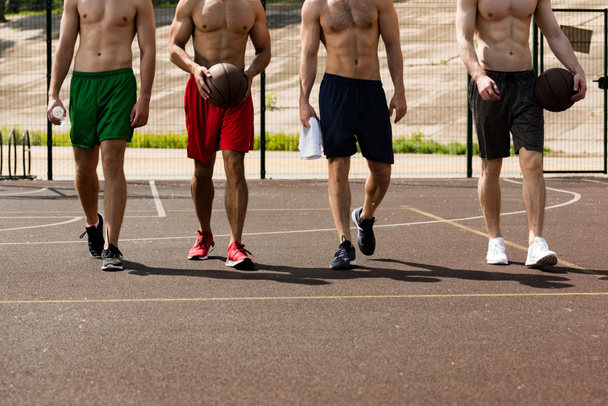 обрезанный вид четырех безрубашечных баскетболистов с мячами на баскетбольной площадке
 - Фото, изображение