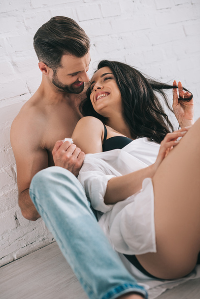 sexy hombre en jeans abrazando con morena y sonriente mujer en el suelo
  - Foto, imagen