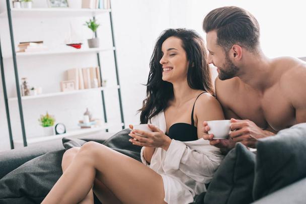 handsome man and attractive woman in bra holding cups and smiling  - Φωτογραφία, εικόνα