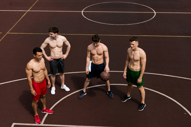 overhead view of four shirtless basketball players with ball at basketball court - Zdjęcie, obraz