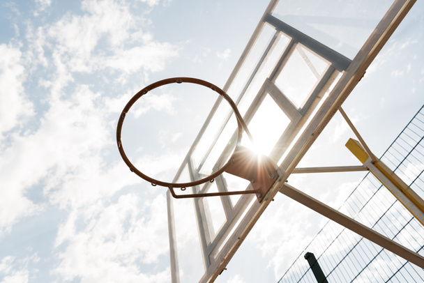 Spodní pohled na basketbalovou desku pod modrou oblohou s mraky za slunečného dne - Fotografie, Obrázek