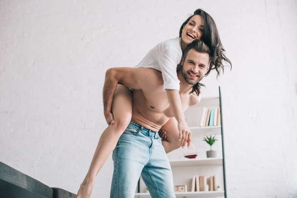 handsome man in jeans and smiling woman in shirt playing and looking at camera  - Foto, Imagem
