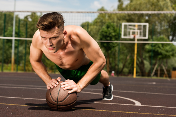 sexy sin camisa deportista haciendo flexiones con pelota en la cancha de baloncesto
 - Foto, Imagen