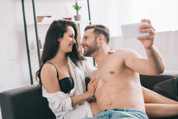 handsome man and sexy woman in shirt and bra looking at each other and taking selfie  - Photo, Image