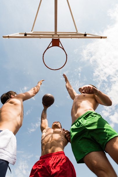 bottom view of shirtless sportsmen playing basketball under blue sky - Fotografie, Obrázek