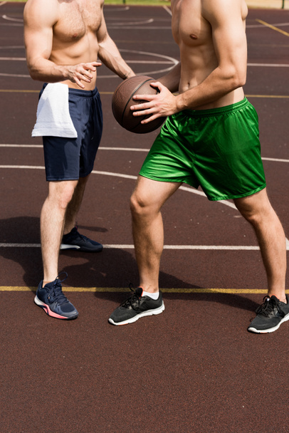 częściowy widok dwóch sportowców torowych grających w koszykówkę na dworze koszykówki w słoneczny dzień - Zdjęcie, obraz