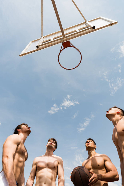 vista inferior de deportistas sin camisa jugando baloncesto bajo el cielo azul
 - Foto, imagen