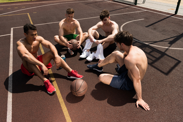 négy fáradt félmeztelen kosárlabda játékos ül kosárlabda bíróság napsütéses napon - Fotó, kép