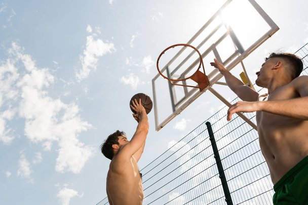 two sexy shirtless sportsmen playing basketball under blue sky at basketball court - Photo, Image