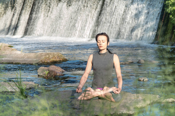 Mädchen macht Yoga im Hintergrund eines Wasserfalls. - Foto, Bild