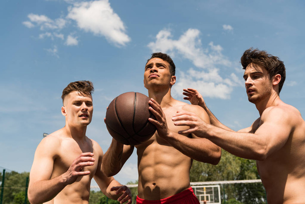 Три сексуальных спортсмена без рубашек играют в баскетбол под голубым небом
 - Фото, изображение