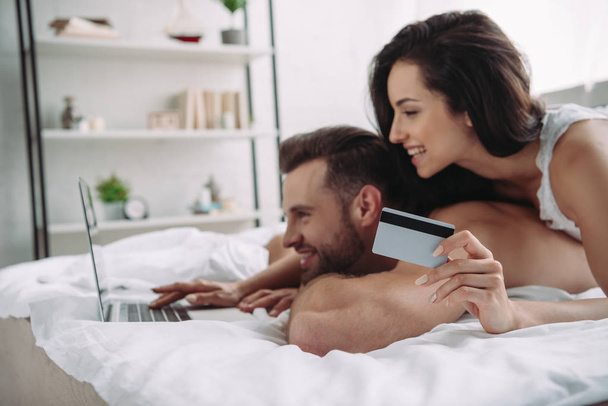beautiful woman holding credit card and handsome man using laptop  - Fotografie, Obrázek