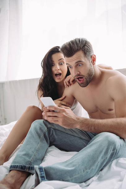 shocked beautiful woman and handsome man looking at smartphone  - Fotografie, Obrázek
