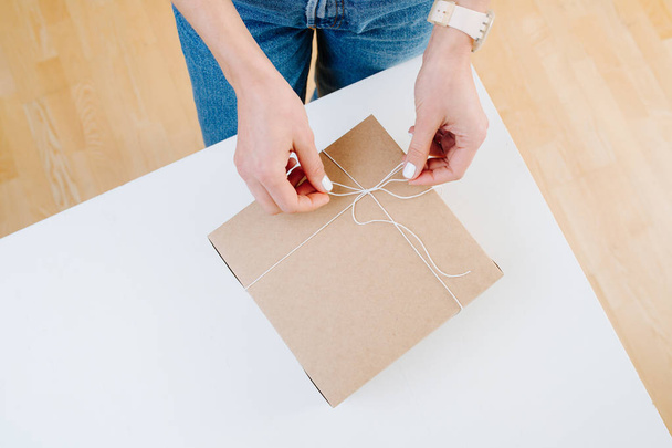 Woman in casual clothes is tying postal cardboard box, making knot at home - Foto, imagen