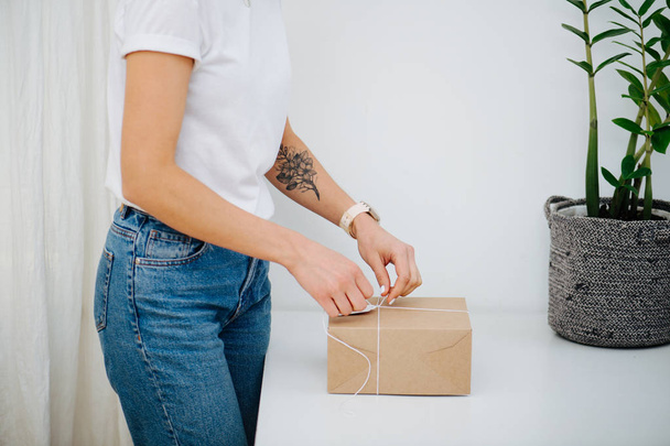 Woman in casual clothes is tying postal cardboard box, making knot at home - Foto, Imagen