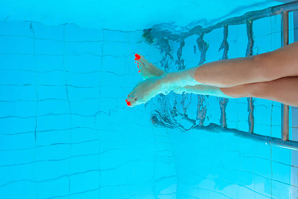 volwassen witte Kaukasische Europese vrouw benen met oranje ultraviolet pedicure onderwater in zwembad - Foto, afbeelding