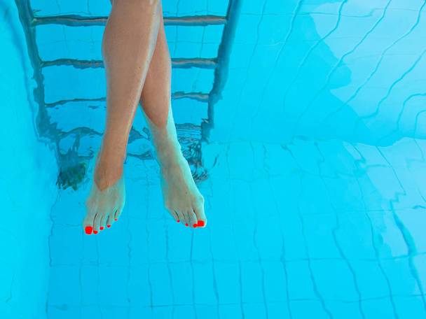 adult white caucasian europian woman's legs with orange ultraviolet pedicure underwater in swimming pool.  Summer. Funny underwater legs in swimming pool, vacation and sport concept. - 写真・画像