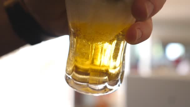 Bliska ręka męskiego barmana trzymania szkła i nalewania lekkiego piwa. Zimny napój alkoholowy grając małe pęcherzyki w kubku. Tło jest defocused. Zwolnionym - Materiał filmowy, wideo