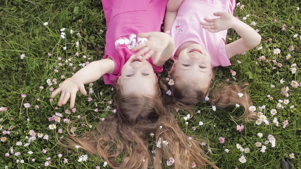 Dois bonito menina deitada de cabeça para baixo na grama prado e flores fazendo beijo de ar e mão acenando
 - Filmagem, Vídeo