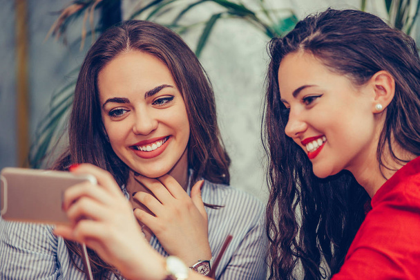 Two young women looking at mobile phone and smiling - Foto, afbeelding