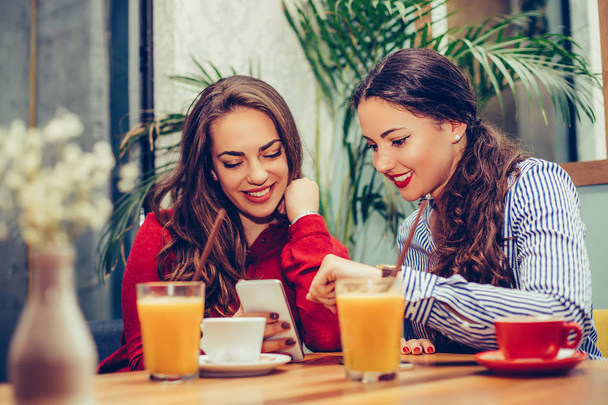 Dwie młode kobiety siedzące w kawiarni, relaks i oglądanie somet - Zdjęcie, obraz