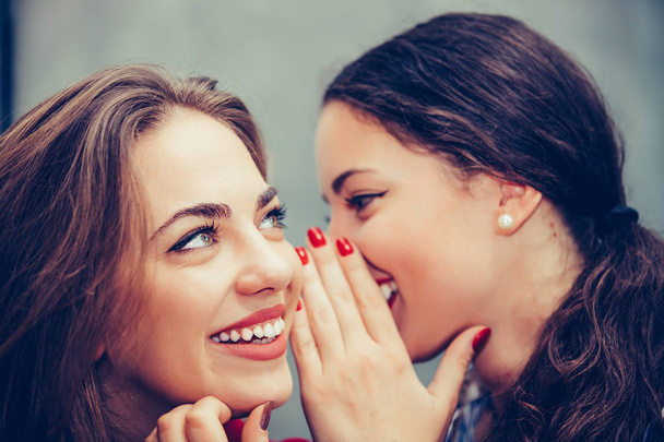 Fiatal szép nő sutkolás valamit barátai fül - Fotó, kép