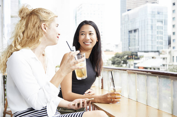Две симпатичные девушки пьют вкусные холодные коктейли и сплетничают в кафе
 - Фото, изображение
