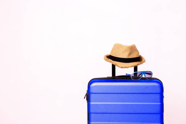 Blue sunglasses and straw summer hat on blue luggage - Fotó, kép
