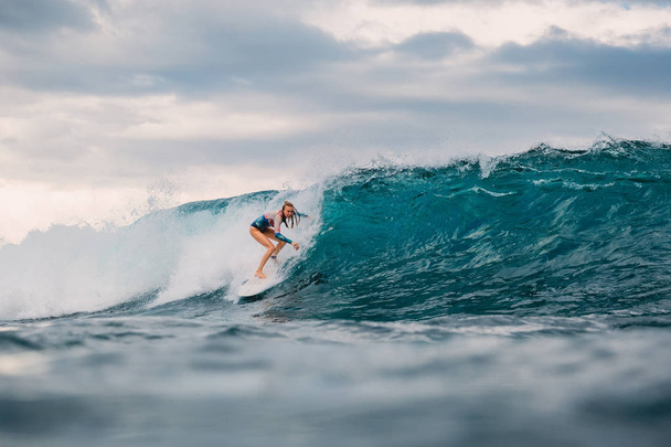 Surffaustyttö surffilaudalla. Surffaaja nainen ja iso sininen aalto
 - Valokuva, kuva
