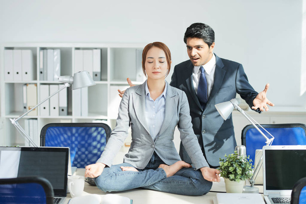 Irritated angry businessman looking at young woman meditating in lotus position - Photo, Image