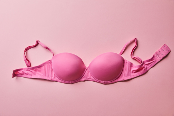top view of pink brassiere on light pink background, breast cancer concept - Foto, afbeelding