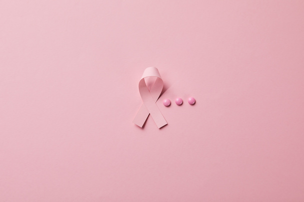 breast cancer ribbon and three pills on light pink background - Фото, зображення