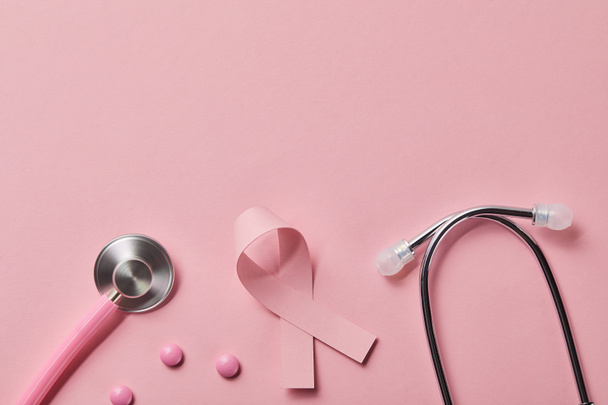 top view of pink metal stethoscope, breast cancer ribbon and three pills on light pink background - Photo, Image