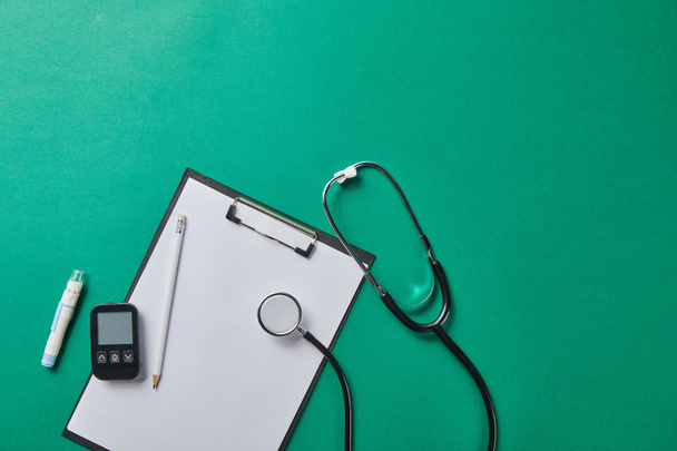 Widok z góry na Lancet krwi i stetoskop pobliżu glukometer i ołówek na folder na zielonym tle - Zdjęcie, obraz