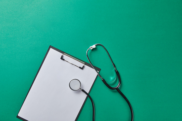 top view of stethoscope near folder with blank paper isolated on green - Photo, Image