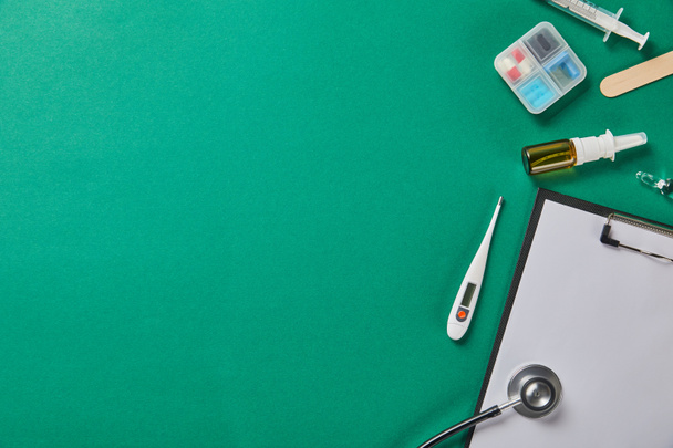 syringe, wooden tongue depressor, ampule, pill box, nasal spray, thermometer, stethoscope and folder on green background - Photo, Image