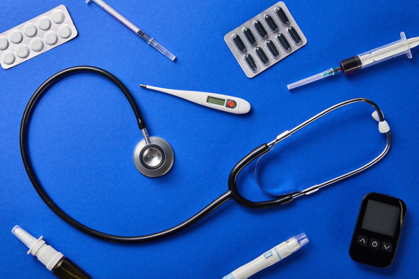 blísters, aerosol nasal, termómetro, lanceta de sangre, glucosímetro, jeringas y estetoscopio sobre fondo azul
 - Foto, Imagen
