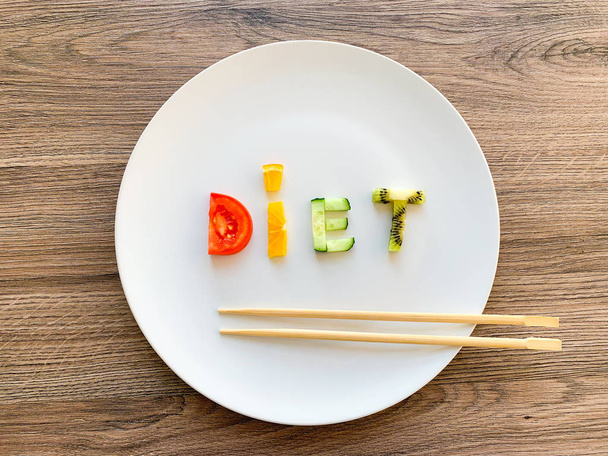 Word Dieet gemaakt van gesneden groenten in witte plaat op houten ondergrond - Foto, afbeelding