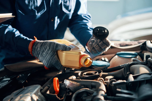 Hands of mechanic pouring a bottle of oil in car engine  - Photo, Image