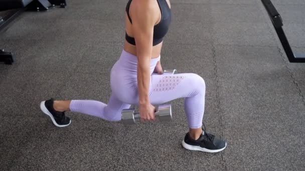 Sportif kadın spor salonunda elinde dambıl ile bacaklar için lunges yapıyor, bacaklar closeup. - Video, Çekim