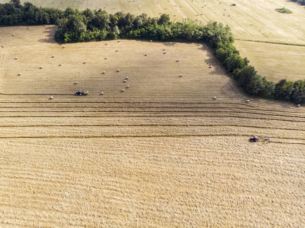 Nature and landscape, aerial view of fields with tractor with round baler and tractor with a rake, machines for collecting and pressing hay. Field with swaths ready to be transformed into round bales - Foto, imagen