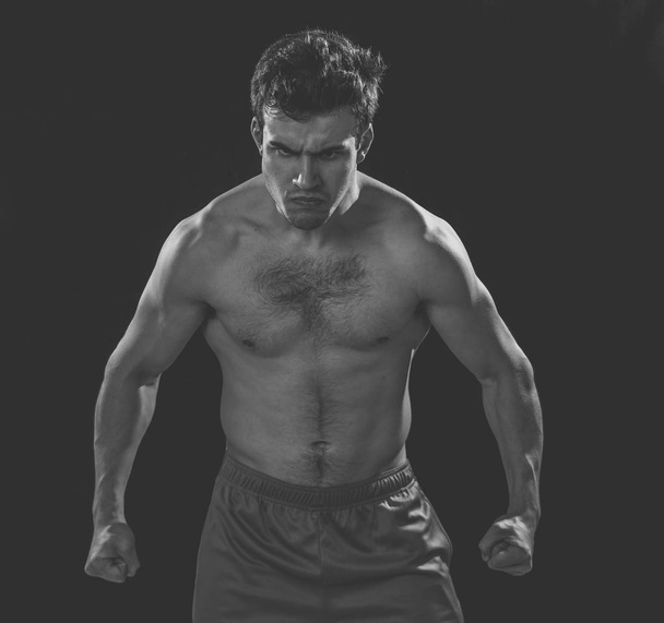 Portrait of strong muscular sports man with an intense furious look. Expressive sexy shirtless angry man looking powerful on black background in Workout, training and fitness concept. - Photo, Image