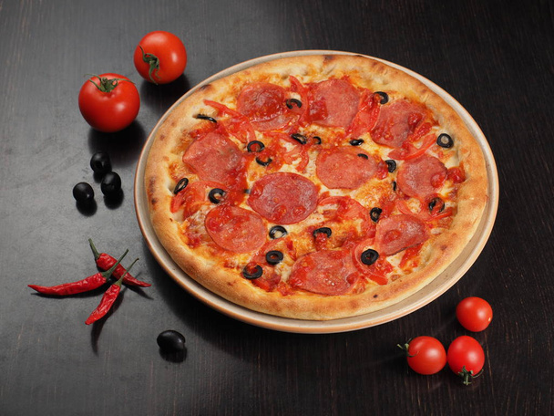 Pizza mit Salami, Tomaten und Oliven auf einem Teller - Foto, Bild